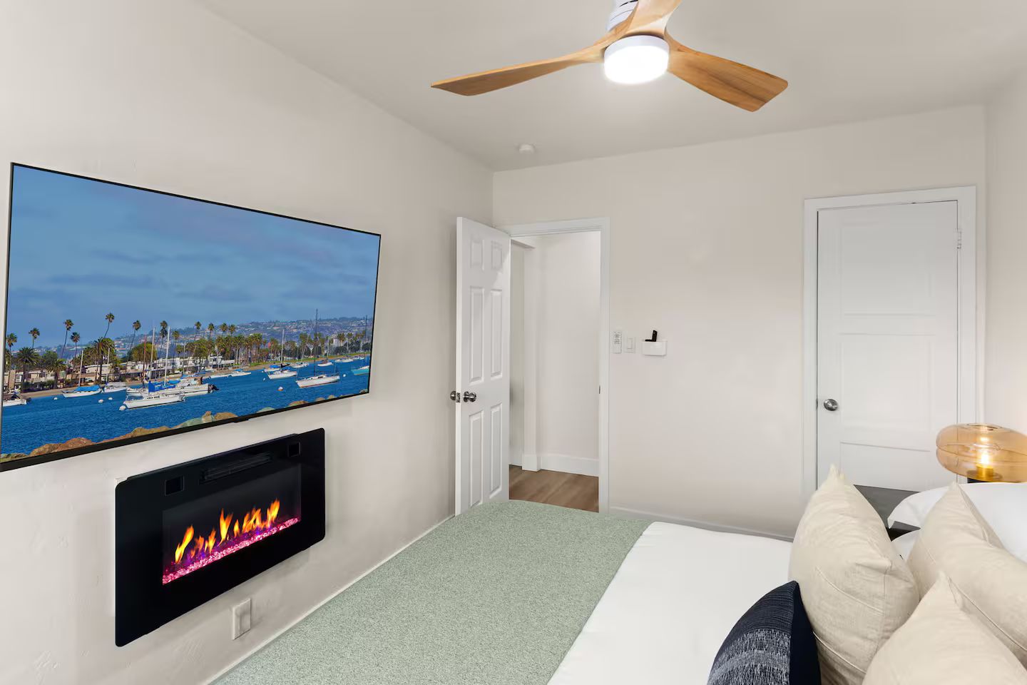 Une chambre avec un téléviseur fixé au mur, un ventilateur de plafond, une cheminée et un lit avec des oreillers.
