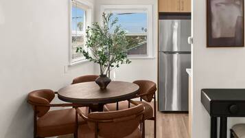 Una cocina compacta con refrigerador de acero inoxidable, una mesa de comedor con cuatro sillas y una planta en el alféizar.