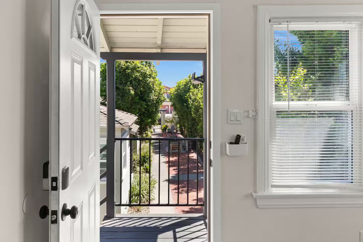 A door leading to a covered outdoor area with a view of a residential street and a window with blinds.
