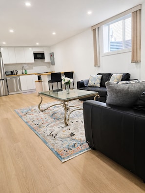 Ein modernes Wohnzimmer mit einem Glastisch, einem schwarzen Sofa und einem gemusterten Teppich.