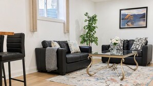 Ett modernt vardagsrum med två svarta soffor, ett soffbord, en krukväxt och en tavla på väggen.