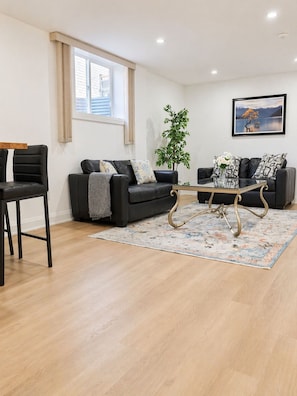 Ein modernes Wohnzimmer mit zwei schwarzen Sofas, einem Couchtisch, einem Blumentopf und einem Bild an der Wand.
