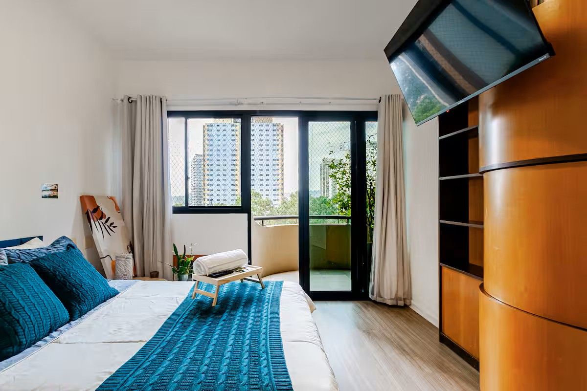Un dormitorio con cama, televisión, balcón y vistas a edificios.