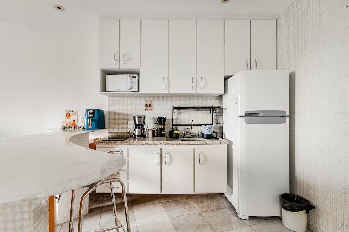 Una cocina con armarios blancos, microondas, cafetera y refrigerador.