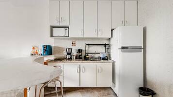 Una cocina con armarios blancos, microondas, cafetera y refrigerador.