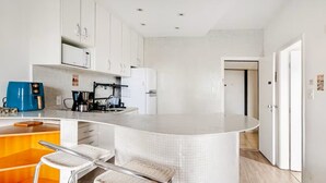 Cozinha moderna com armários brancos, uma ilha curva e dois banquetas de vime.