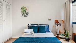 Quarto com cama, mesa de cabeceira e planta em vaso.