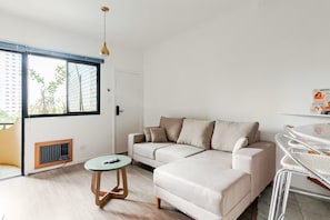 A modern living room with a sectional sofa, a round coffee table, and a dining area with a metal chair. - Apartment with heated pool and gym in Alphaville - Barueri - São Paulo (Barueri)