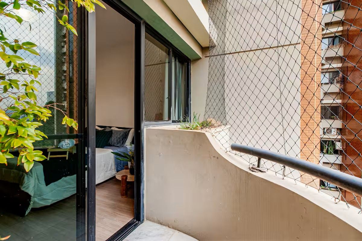 A balcony with a metal railing, a small seating area, and a view of a building in the background.