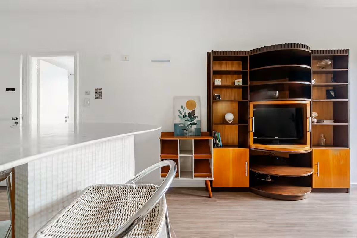 Una sala moderna con una unidad de entretenimiento curva de madera, un televisor de pantalla plana y una silla de mimbre.