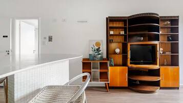 Una sala moderna con una unidad de entretenimiento curva de madera, un televisor de pantalla plana y una silla de mimbre.