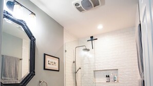 Een moderne badkamer met een wit wastafelmeubel, een grote spiegel, een toilet, een douche met glazen deur en een betegelde wand in het wit.