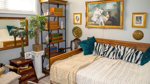 Een slaapkamer met een bed, een boekenkast, een schilderij en een raam.