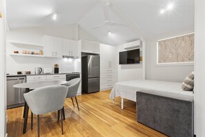 Eine moderne Küche mit weißen Schränken, einem Edelstahlkühlschrank und einem Essbereich mit grauem Stuhl und Tisch.