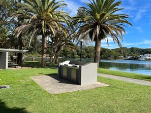 Ein Park mit einer Beton-Sitzgelegenheit, Palmen und einem See.