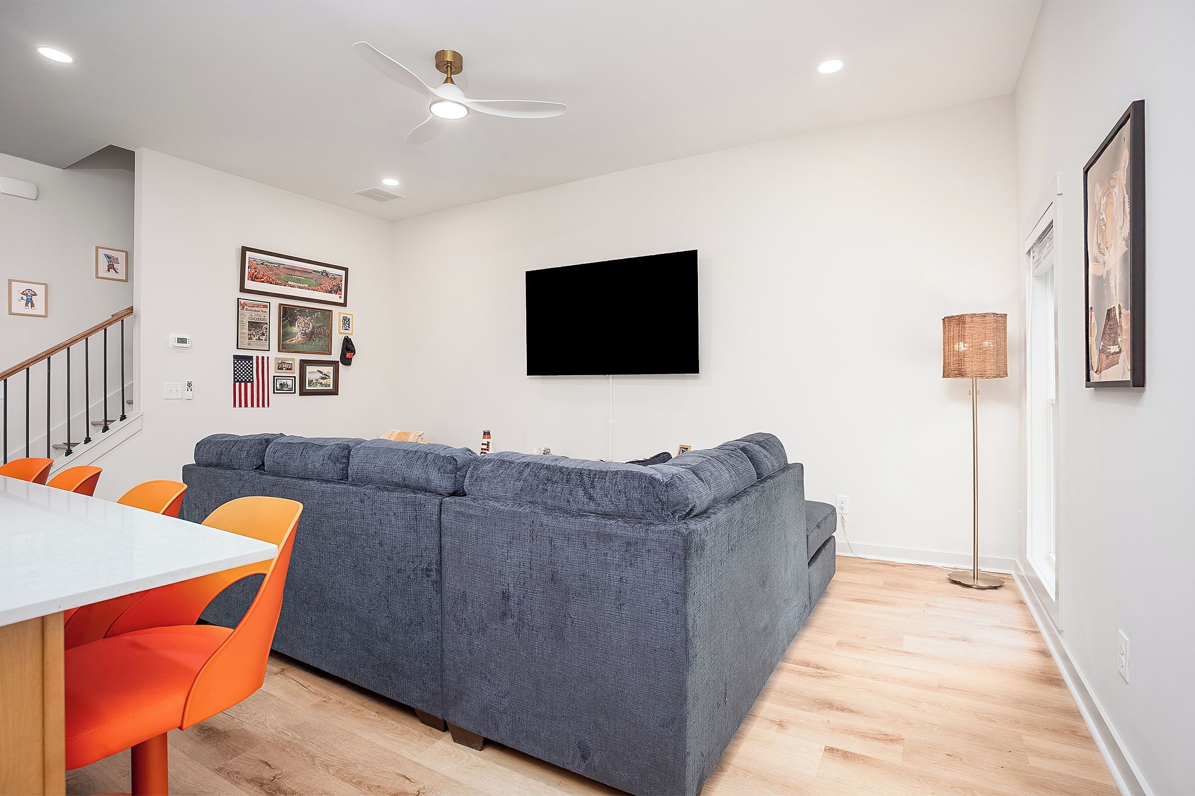Ein modernes Wohnzimmer mit einem grauen Sofa, orangenen Sesseln, einem weißen Tisch und einem an der Wand befestigten Flachbildfernseher.