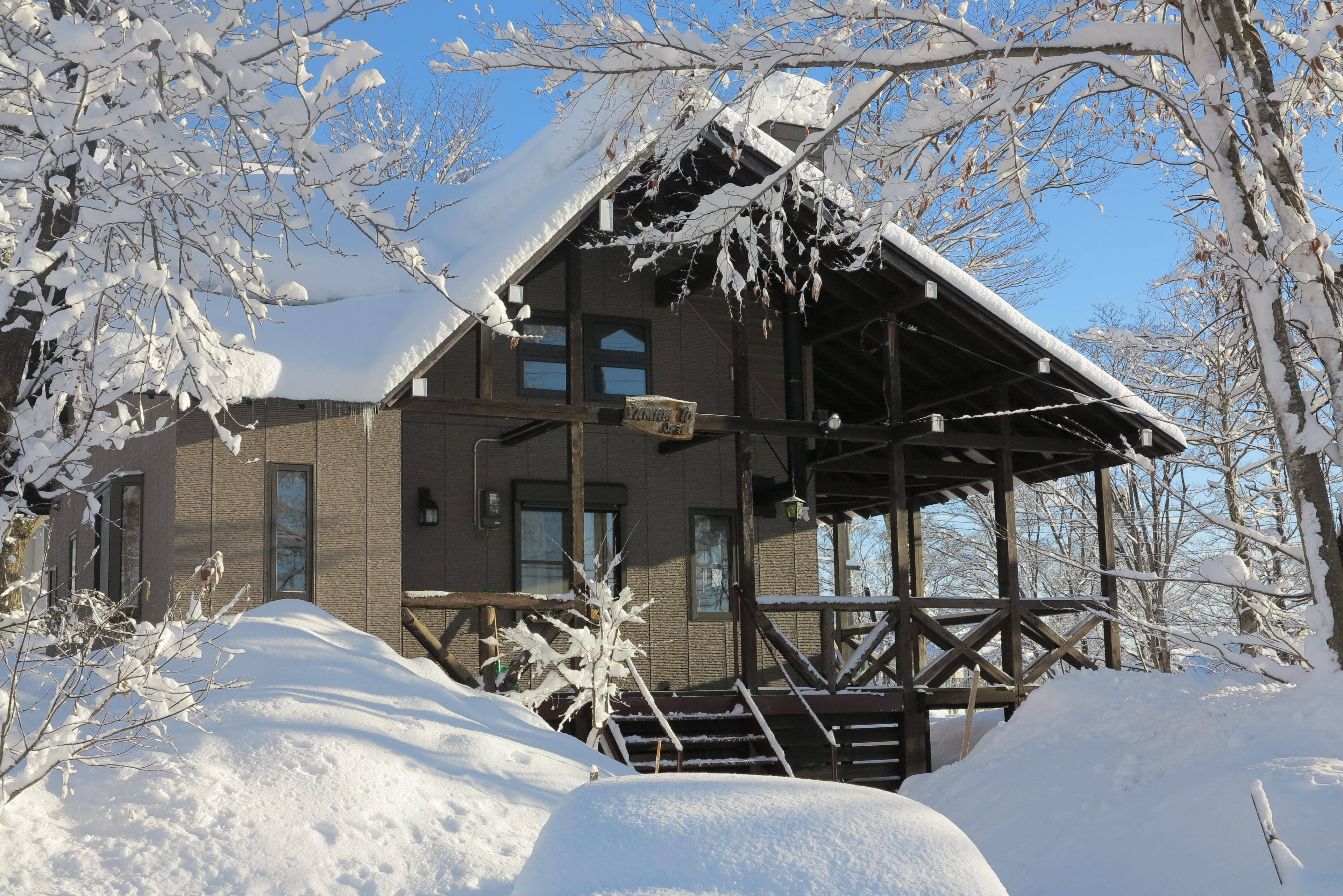 A wooden cabin with a covered porch, surrounded by snow-covered trees.