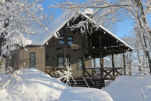 A wooden cabin with a covered porch, surrounded by snow-covered trees. - Sakura Lodge Myoko - 3 min drive to Akakura Onsen (Myoko)
