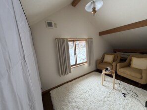 A room with a window, a ceiling fan, a white fluffy rug, and a beige sofa.