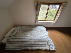 A room with a single bed, a window with curtains, and wooden flooring.