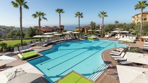 A large outdoor swimming pool with multiple lounge areas, palm trees, and a view of the ocean. - Resort with 2 bedrooms and AC in perfect Newport Coast (newport Coast)