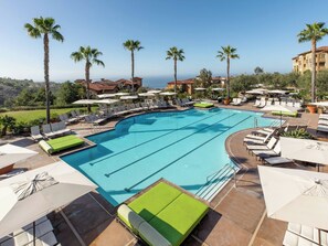 A large outdoor swimming pool with multiple lounge areas, palm trees, and a view of the ocean. - Resort with 2 bedrooms and AC in perfect Newport Coast (newport Coast)