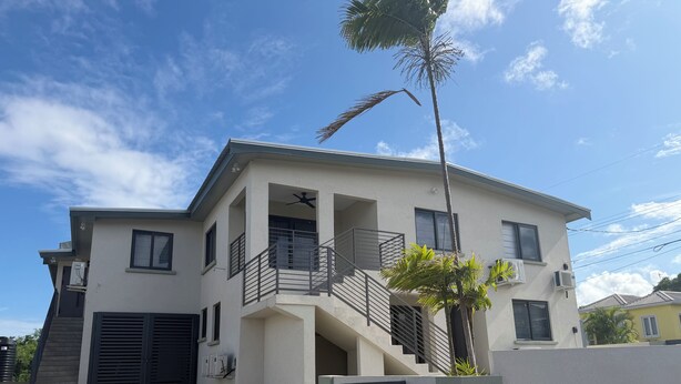 A two-story building with a balcony, a staircase, and a palm tree. - 2 bed 1 bath apartment w/ AC, WIFI, kitchen & 5 min walk to west coast beaches (Appleby)