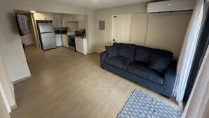 A compact living space with a kitchenette, a sofa, and a patterned rug. - 2 bed 1 bath apartment w/ AC, WIFI, kitchen & 5 min walk to west coast beaches (Appleby)