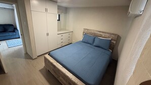 A bedroom with a wooden bed frame, a wardrobe with multiple drawers, a mirror, and a ceiling light. - 2 bed 1 bath apartment w/ AC, WIFI, kitchen & 5 min walk to west coast beaches (Appleby)