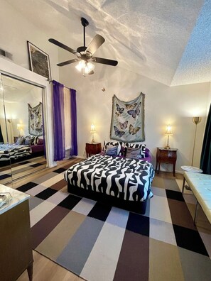 A bedroom with a bed, a ceiling fan, a window with purple curtains, a wall-mounted painting, and a bedside table with a lamp. - Artsy Townhome / Pool & Spa / Attached Garage / North Hollywood (Los Angeles)