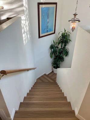 A wooden staircase with a handrail, a potted plant, a framed artwork, and a hanging light fixture. - Artsy Townhome / Pool & Spa / Attached Garage / North Hollywood (Los Angeles)