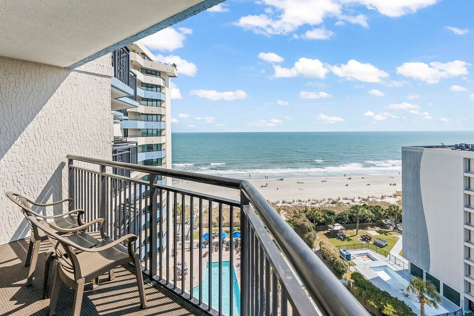 Un balcon avec vue sur la plage et l’océan, une piscine et un immeuble à plusieurs étages.