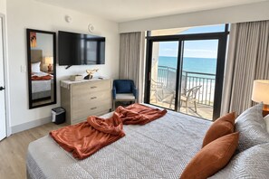 A hotel room with a bed, a dresser, a TV, a balcony with a view of the sea, and a chair. - Family-Friendly 3BR | Indoor Pools & Arcade (Myrtle Beach)