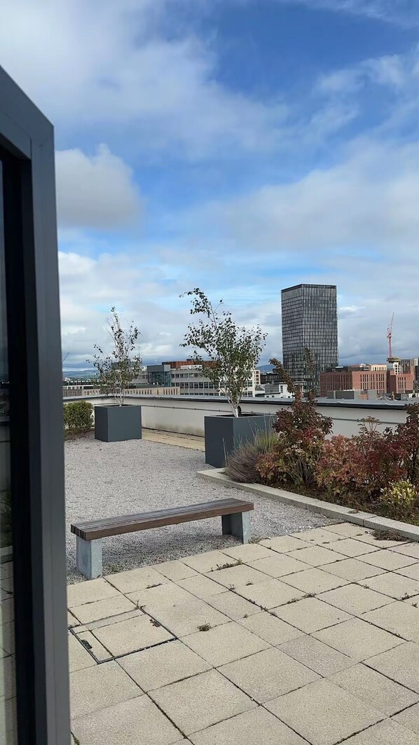 Eine Terrassenanlage im Freien mit einer Bank, Topfpflanzen und Blick auf eine Stadtlandschaft, einschließlich eines hohen Gebäudes.
