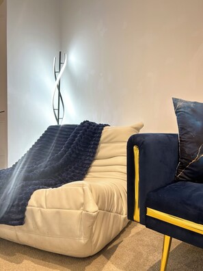 Ein Zimmer mit einer Couch und einem Sessel, einer Wandleuchte sowie einem Teppichboden.