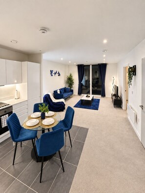 Ein modernes Wohnzimmer mit Essbereich, ausgestattet mit einer Couch, Sesseln, einem Couchtisch und einer Küchenzeile mit Schränken und Herd.
