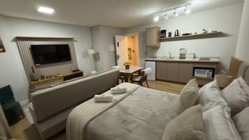 A modern hotel room with a bed, a TV, a kitchenette, and a dining area.