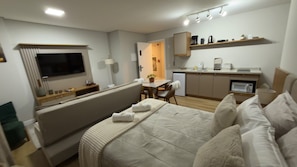 Ett modernt hotellrum med en säng, en TV, ett litet kök och en matplats.