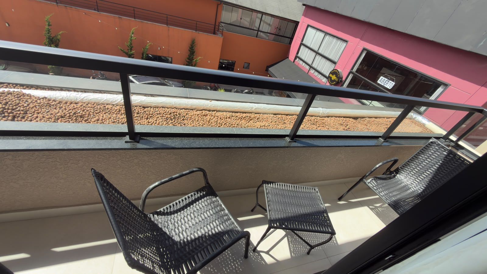 A balcony with two chairs and a railing, overlooking a building with a pink facade and a sign that reads 'ABERTO'.