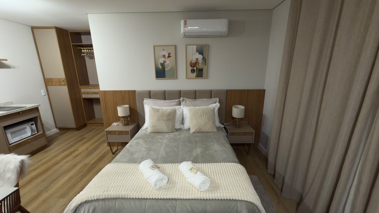 A hotel room with a bed, bedside tables, a wardrobe, and an air conditioning unit.