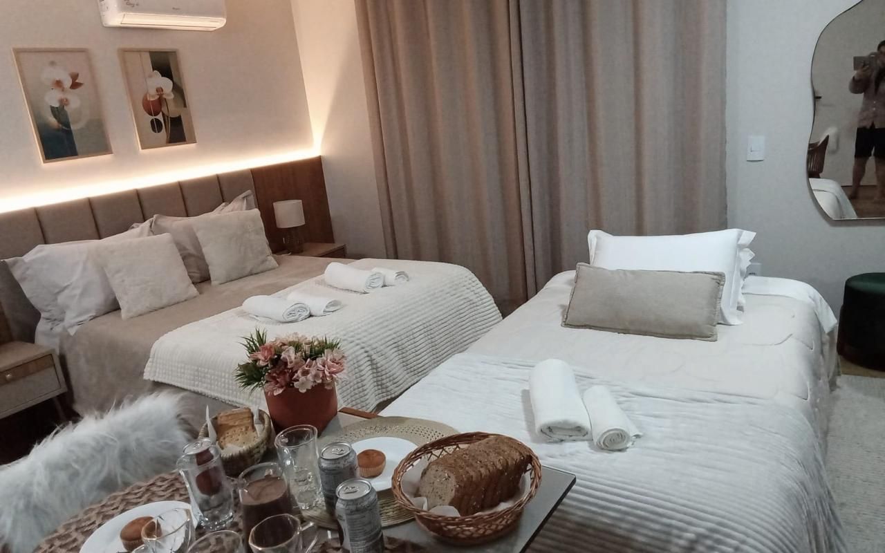 A hotel room with two beds, a bedside table with a lamp, a mirror, and a wall-mounted air conditioner.
