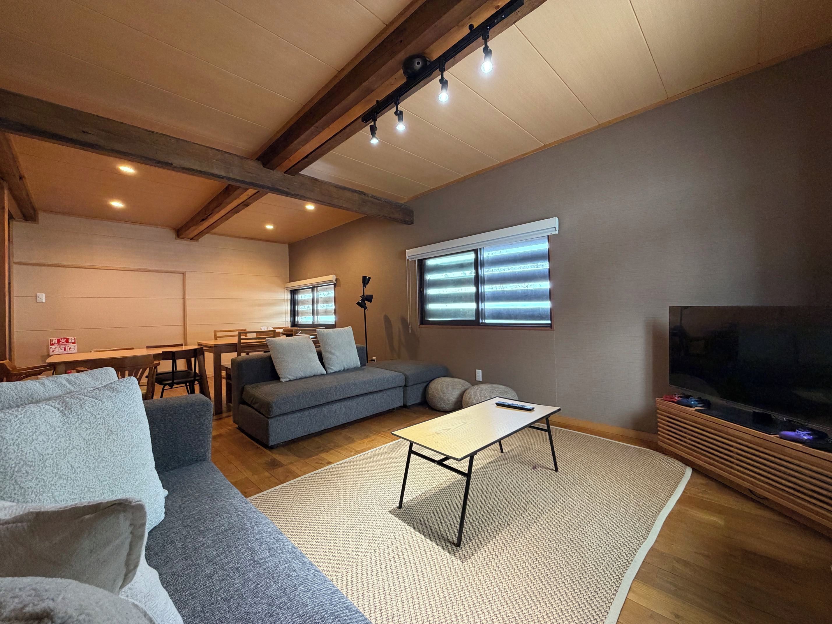 A living room with a sofa, a coffee table, a TV, and a dining area with a table and chairs.