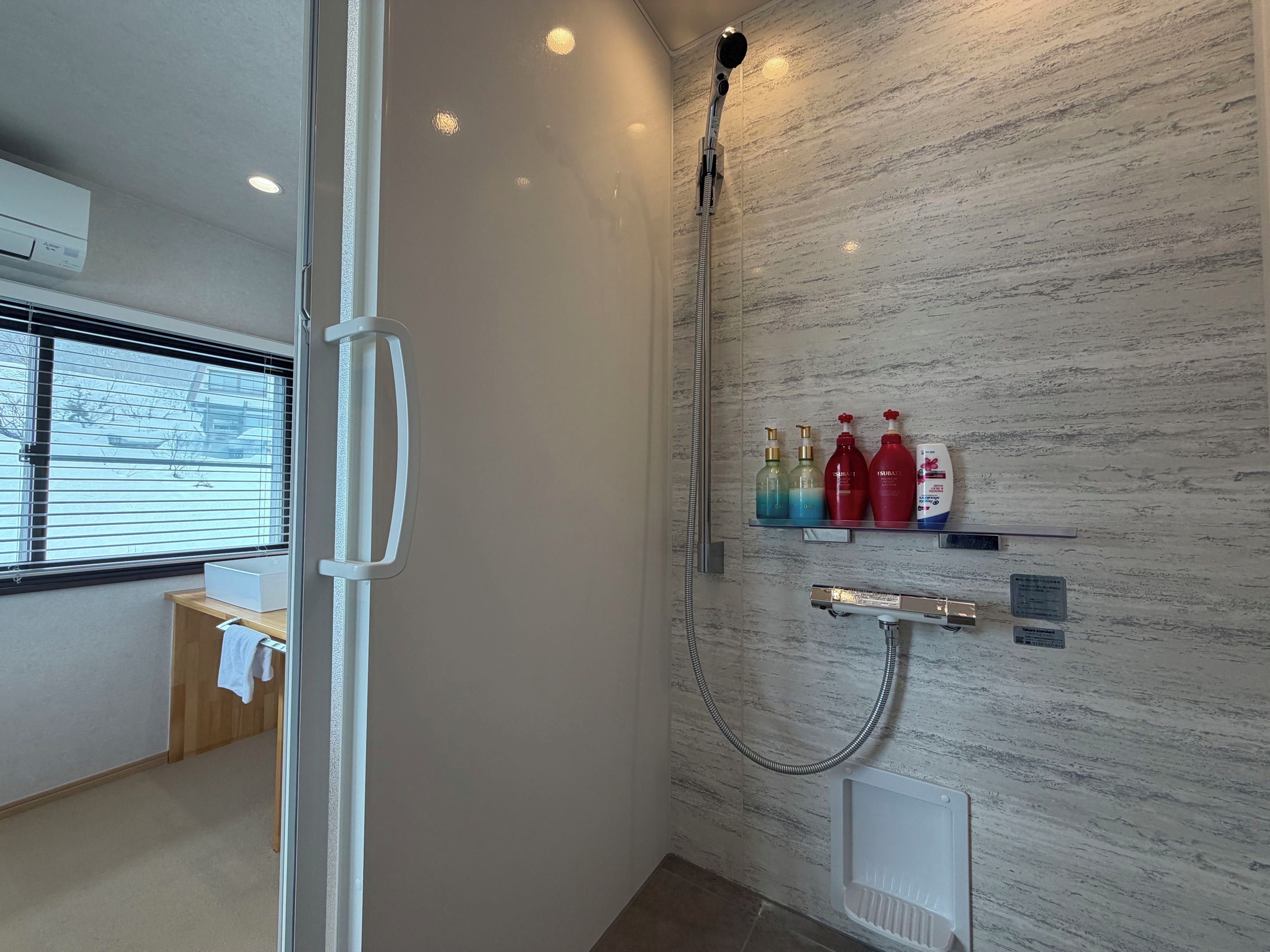 A bathroom with a shower, a towel rack, and a shelf with toiletries.