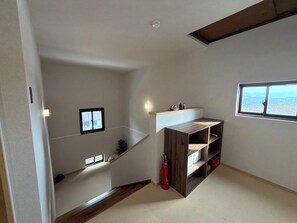 A room with a wooden staircase, a window with a view, and a shelf unit.