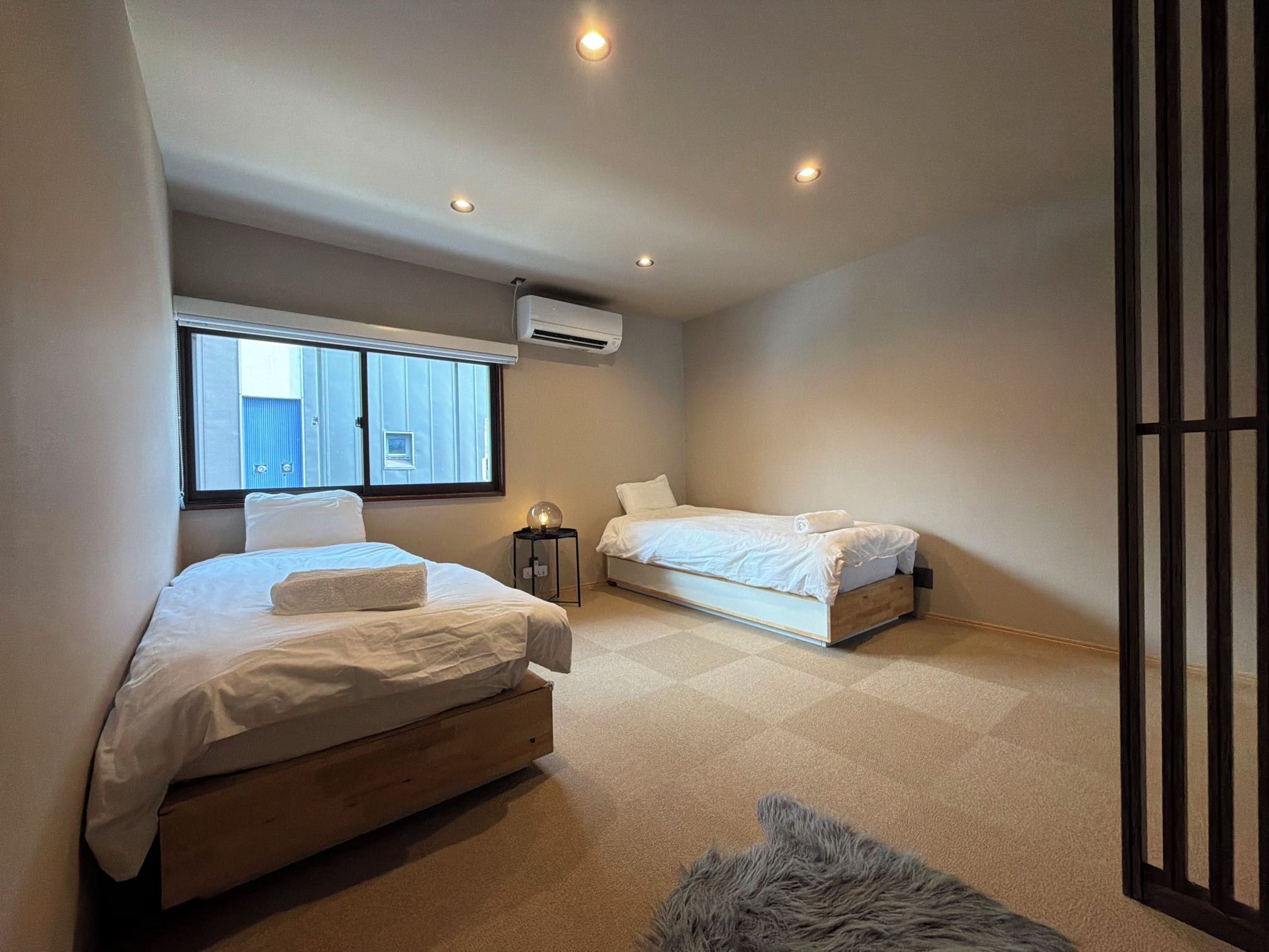 A bedroom with two beds, a window, an air conditioning unit, and a small rug.