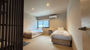 A bedroom with two beds, a window, an air conditioning unit, and a wooden partition.