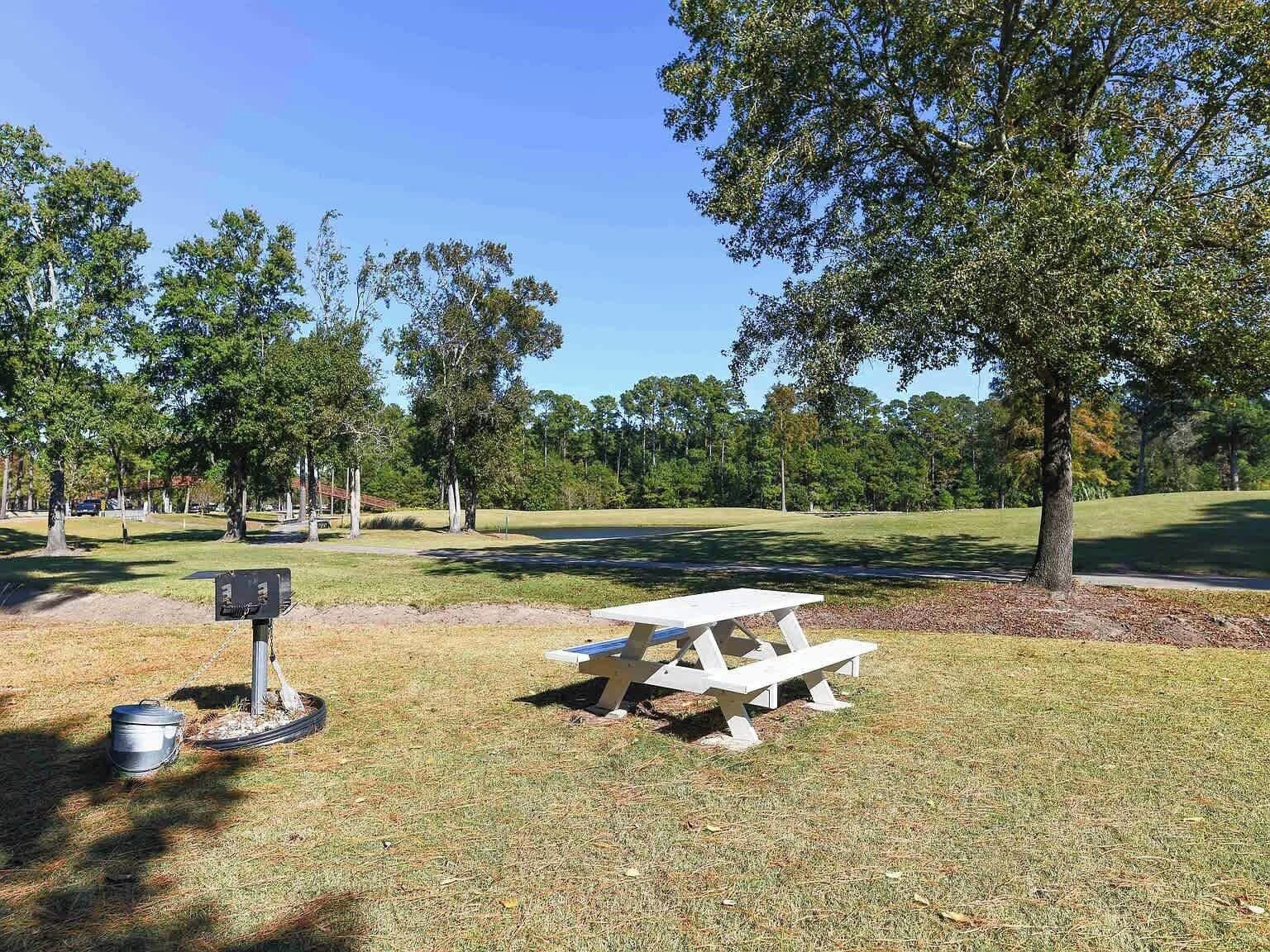 A picnic area with a table and benches, surrounded by trees and a golf course in the background.
