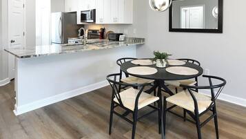 Una cocina moderna con armarios blancos, una isla central con encimera de mármol y una zona de comedor con una mesa redonda y sillas.