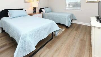 A bedroom with two beds, a nightstand, a lamp, a desk, and a window.