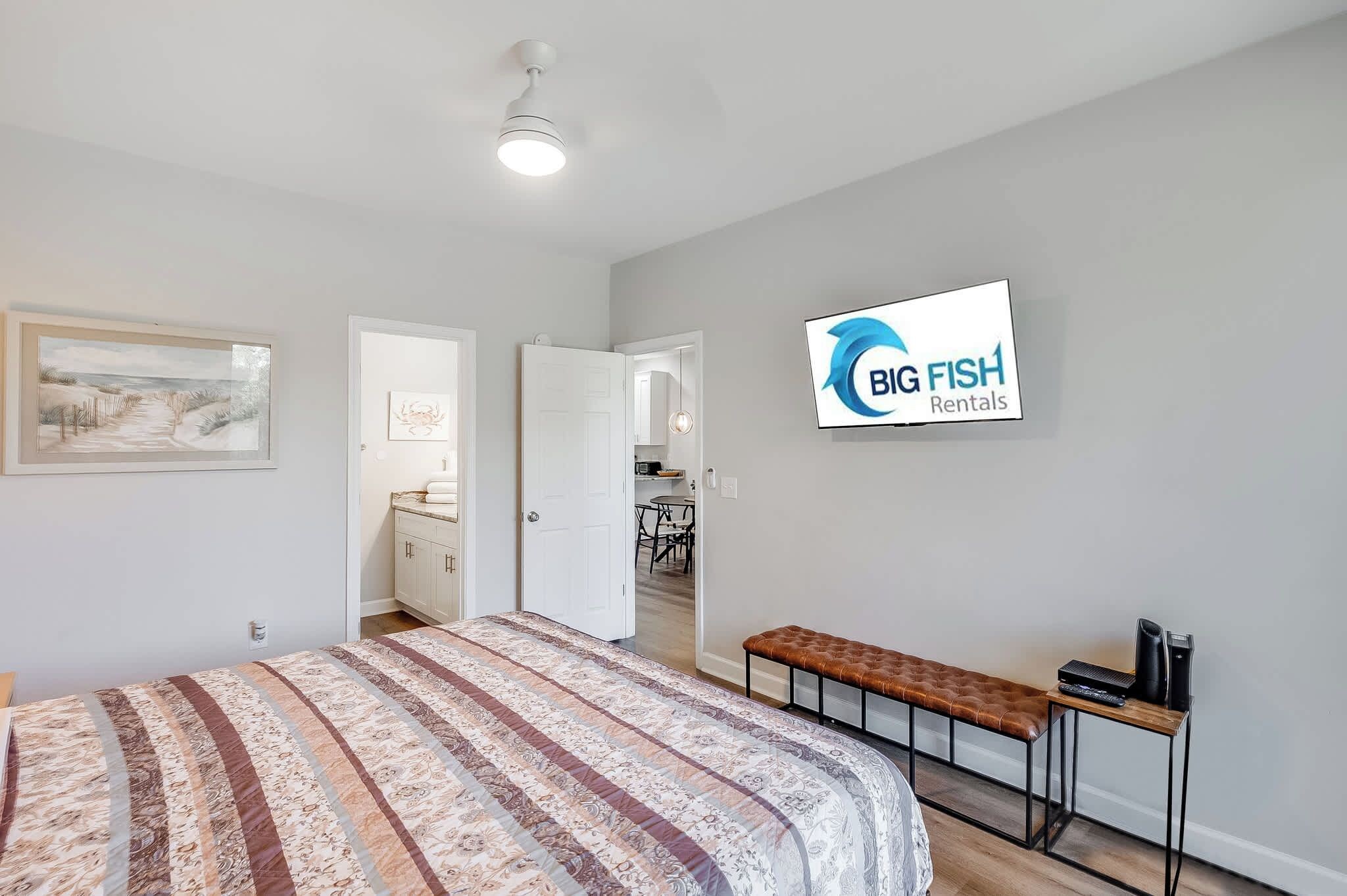 A bedroom with a bed, a bench, a desk with a computer, and a TV displaying 'BIG FISH Rentals'.